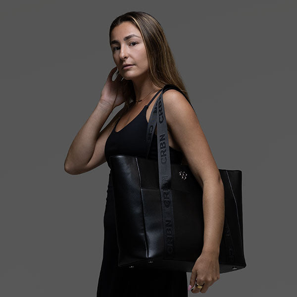 Woman in a black top holds a large black CRBN Club Pickleball Tote with a branded shoulder strap