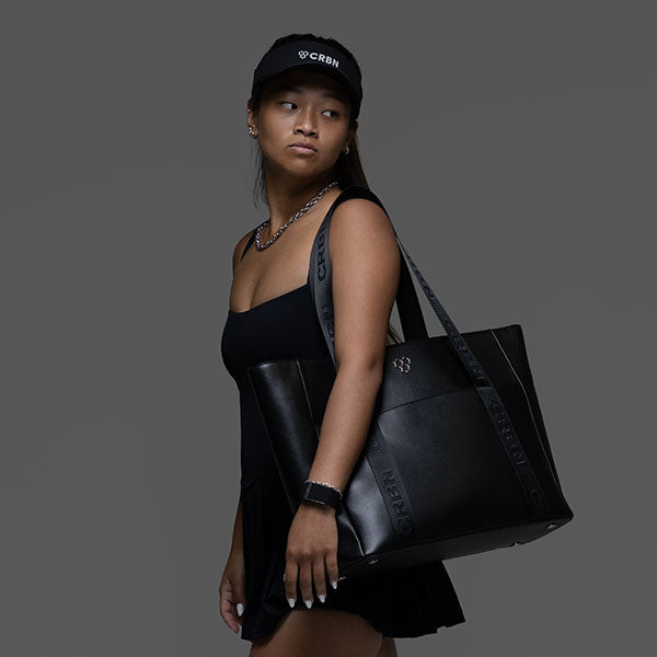 Woman in black carries a black CRBN Club Pickleball Tote with a branded shoulder strap