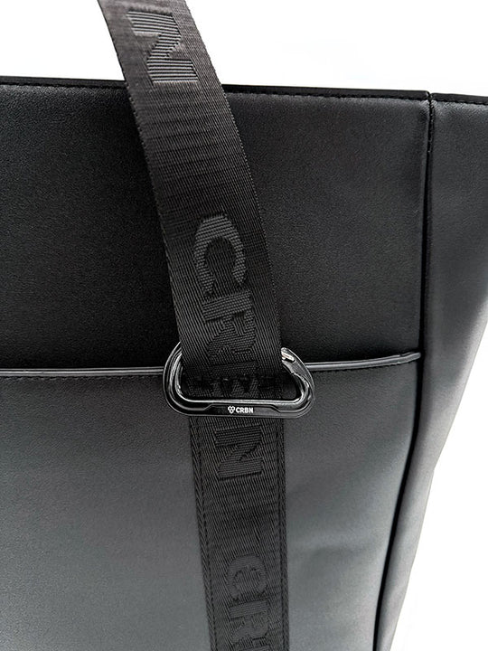Close-up of the black tote with a CRBN branded strap threaded through a metal ring.
