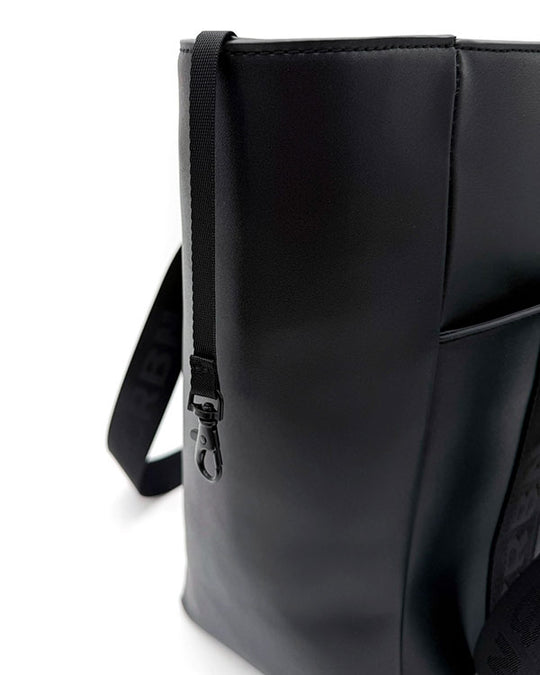 Side profile of the CRBN Club Pickleball Tote featuring a slim zip pocket and sturdy strap attachment on black material